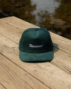 Green cap with 'Tremont' logo on a wooden dock by water